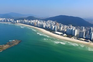 Vue aérienne d’une ville côtière avec de hauts immeubles, une plage et des montagnes en arrière-plan.