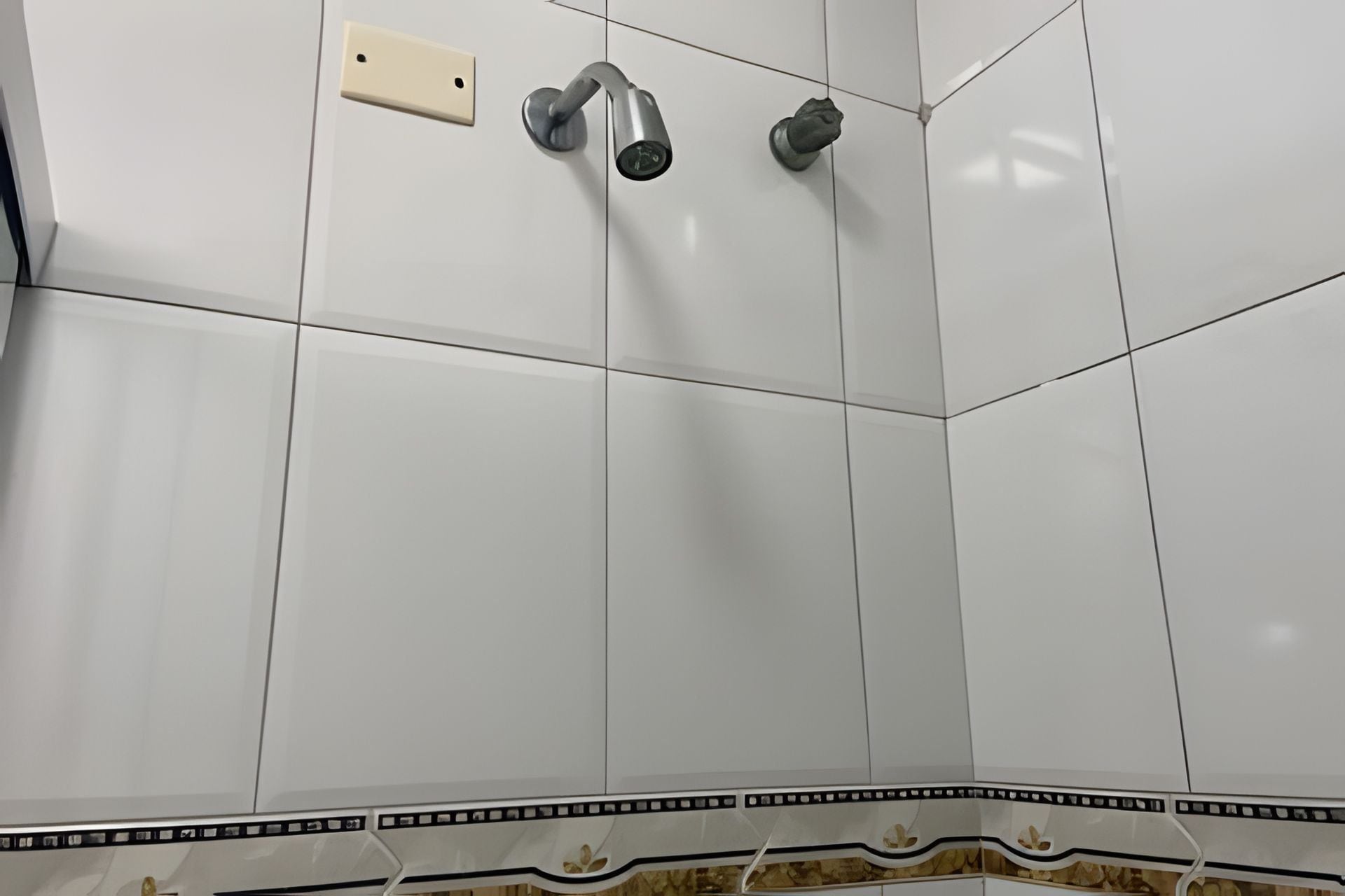 A bathroom with white tiled walls, a shower with a handheld showerhead, and a wall-mounted faucet.
