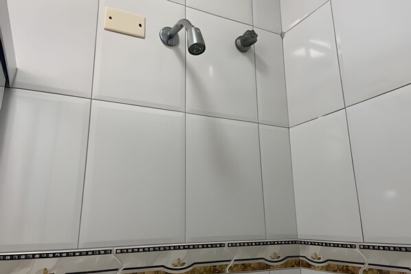 Ein Badezimmer mit weißen Fliesen, einer Dusche inklusive Handbrause und einem am Wand montierten Wasserhahn.