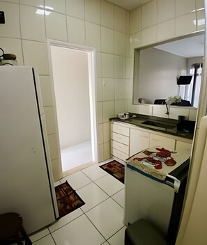 Eine kleine Küche mit weißen Fliesen, einem Kühlschrank, einer Spüle und einer Arbeitsplatte.