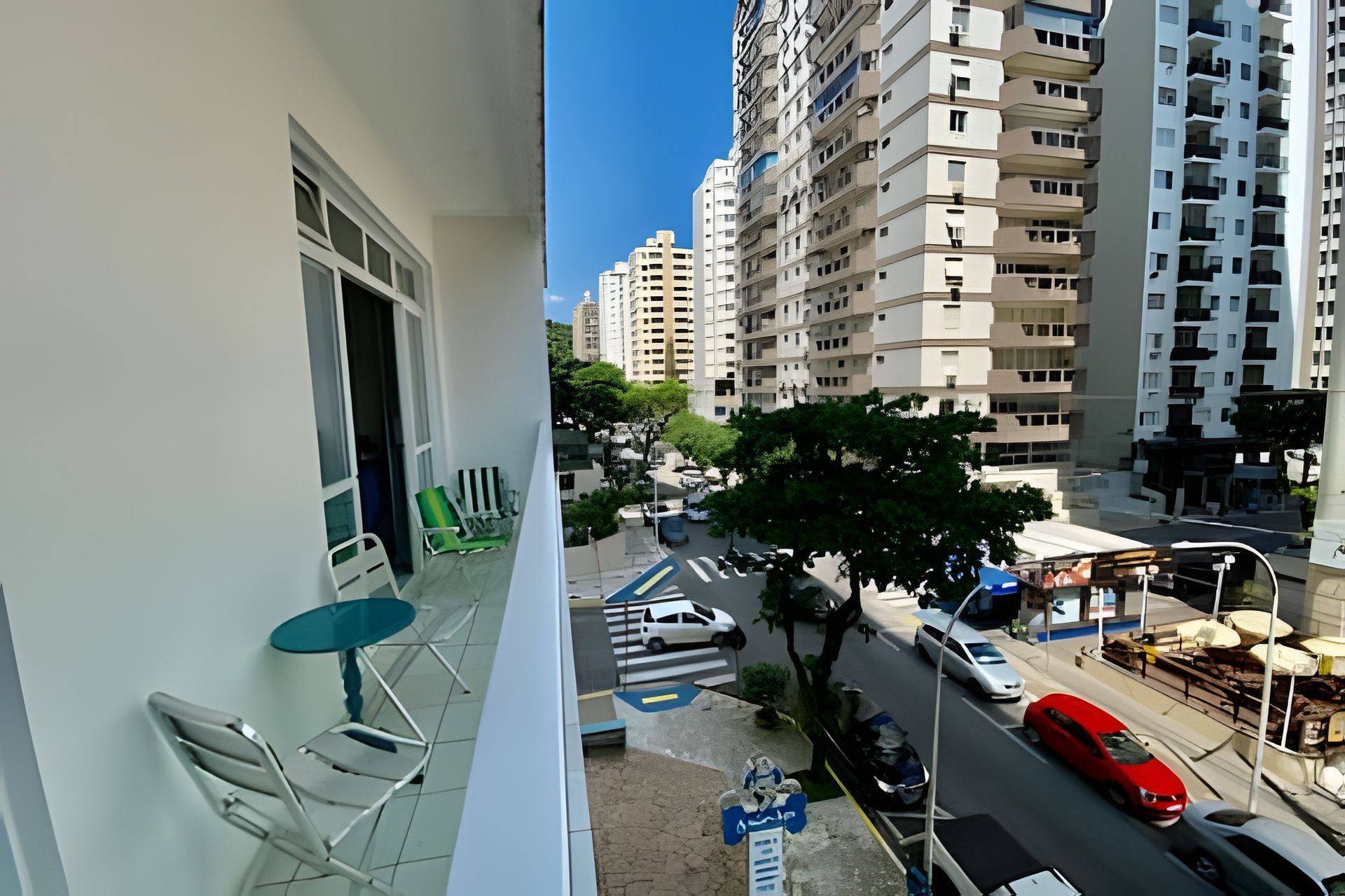 A balcony with a table and chairs, overlooking a street with cars and a tree.