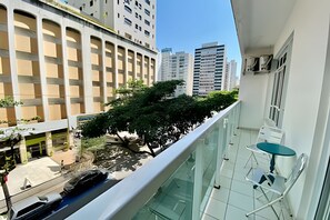 A balcony with a glass railing overlooking a street with cars and buildings.