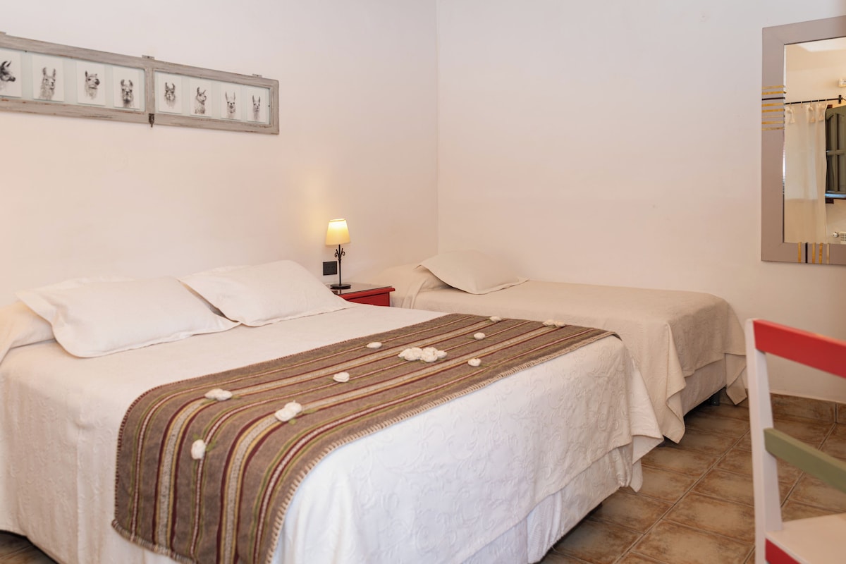 Een hotelkamer met twee bedden, een nachtkastje met lamp, een lijst met afbeelding en een spiegel.