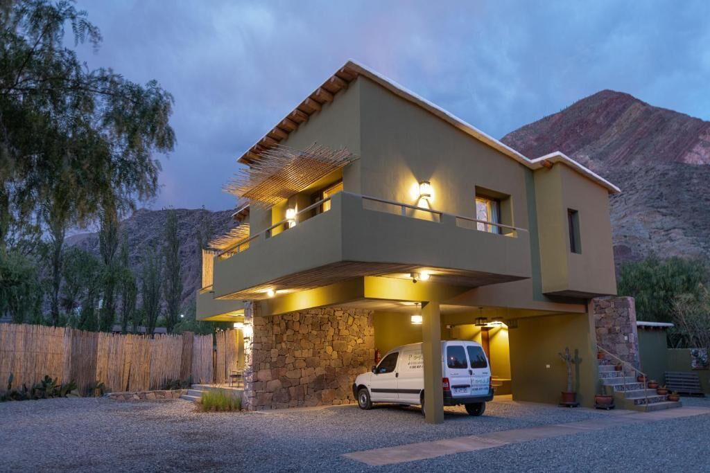 Un edificio de dos pisos con base de piedra, una zona de estacionamiento techada y un vehículo en su interior.