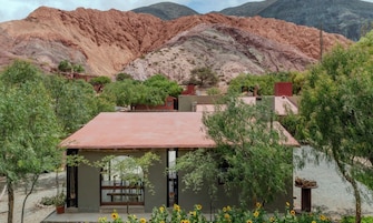 Un edificio de techo rojo, rodeado de vegetación y montañas al fondo.