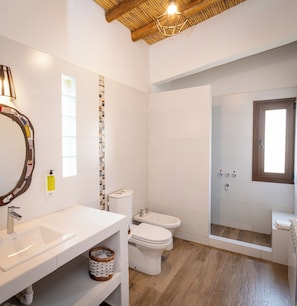Een badkamer met een wit wastafel, toilet en bidet, een douchegedeelte en een houten plafond.