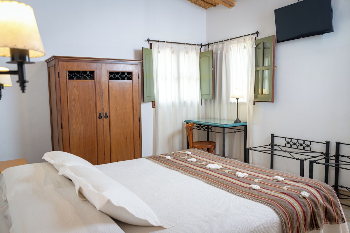 Een slaapkamer met een bed, een houten kast, een bureau, een stoel en een televisie aan de muur.