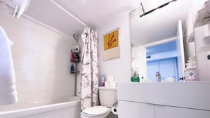 A modern bathroom with a bathtub, toilet, and a shower curtain. There are toiletries on a shelf and a mirror above the sink. - City Central Residences Downtown Toronto (Toronto)