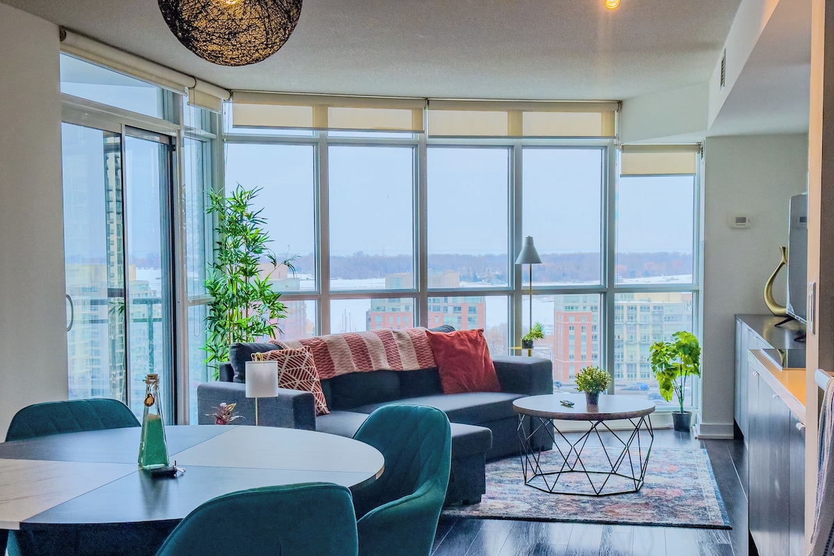 A modern living room with a large window, a sofa, a dining table, and a kitchen area.