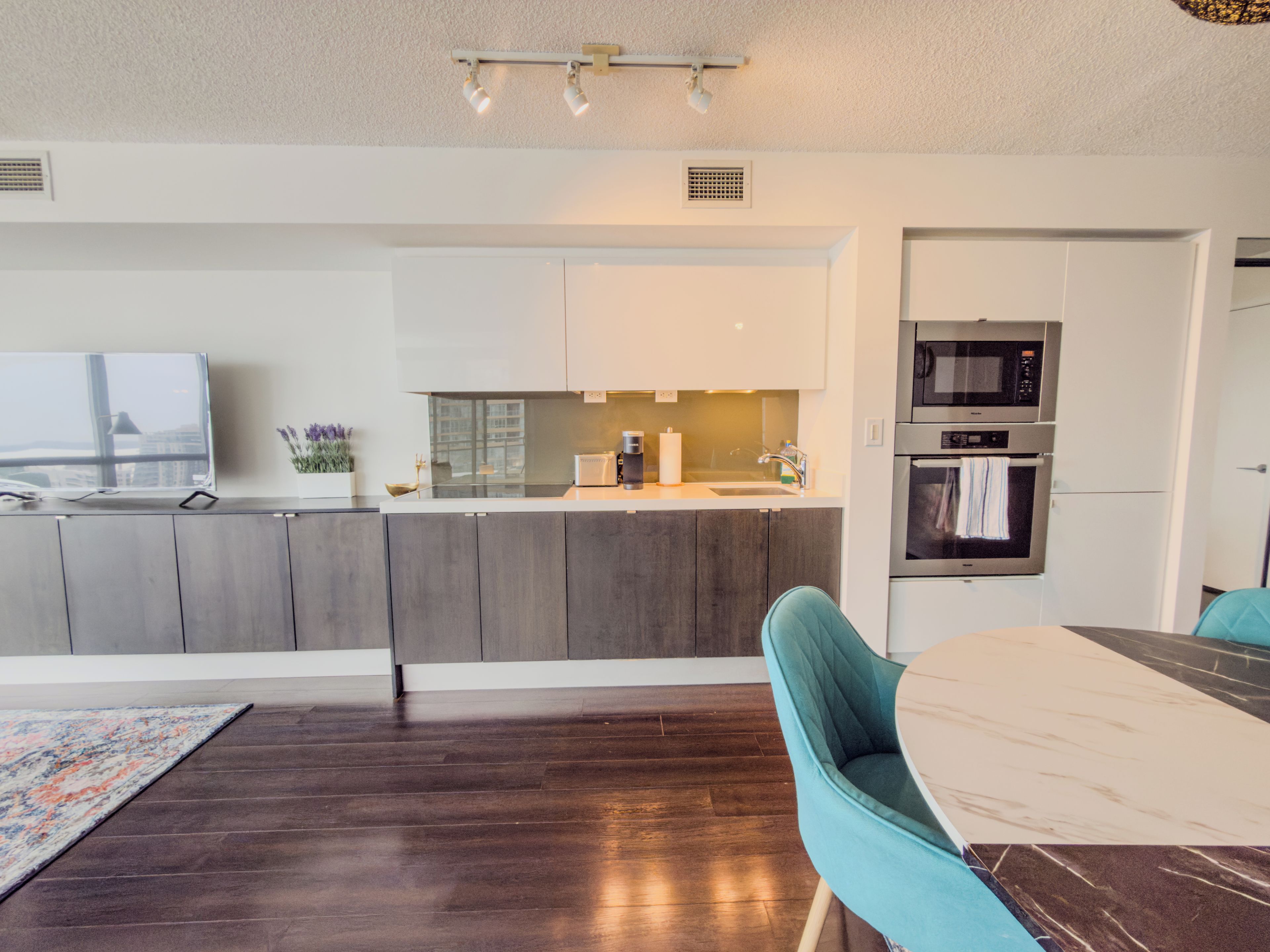 A modern kitchen with a dining area, featuring a large window, built-in appliances, and a wooden floor.