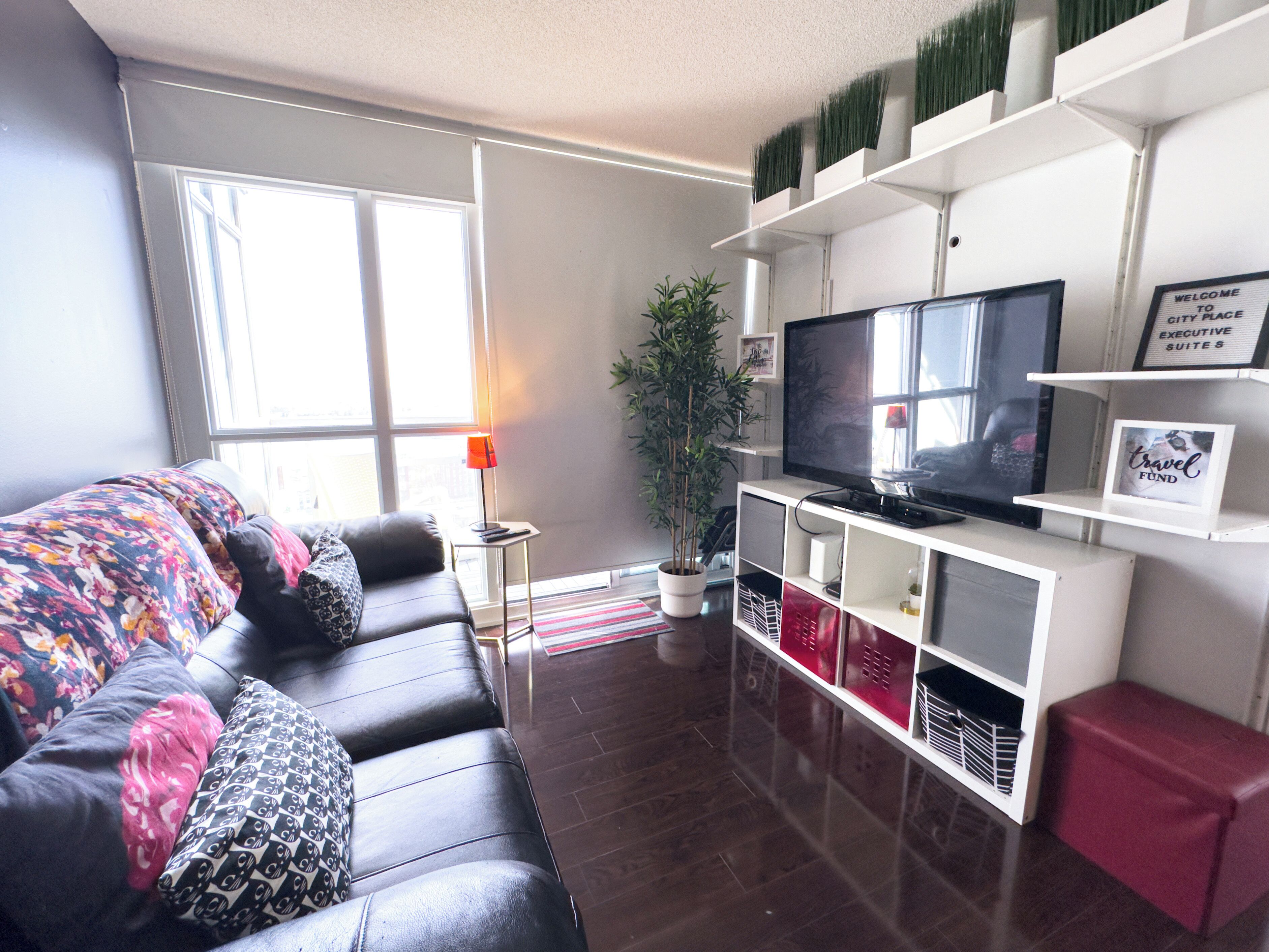 Una sala de estar moderna con un sofá de cuero, un televisor de pantalla plana, una planta en maceta y un reposapiés rojo.