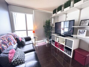 A modern living room with a leather sofa, a flat-screen TV, a potted plant, and a red ottoman. - City Central Residences Downtown Toronto (Toronto)