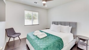 Quarto de hotel com cama, poltrona, mesa pequena, ventilador de teto e janela.