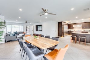 A modern kitchen with dark cabinetry and a central island, a dining area with a wooden table and chairs, and a living room with a sofa and a decorative wall piece. - Private Backyard Oasis-Pool/Bocci/Golf (Palm Springs)