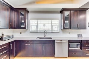 A modern kitchen with dark wood cabinets, a stainless steel sink, a built-in microwave, and a toaster. - Private Backyard Oasis-Pool/Bocci/Golf (Palm Springs)
