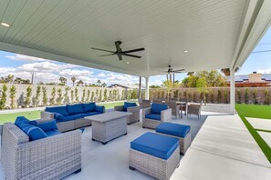 An outdoor patio with wicker furniture, ceiling fans, and a view of a green lawn and distant buildings. - Private Backyard Oasis-Pool/Bocci/Golf (Palm Springs)