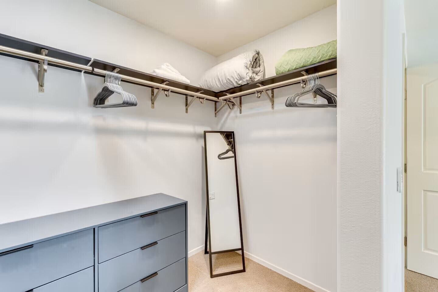 Um closet amplo com barra de espelho, uma cômoda cinza e um cabideiro.