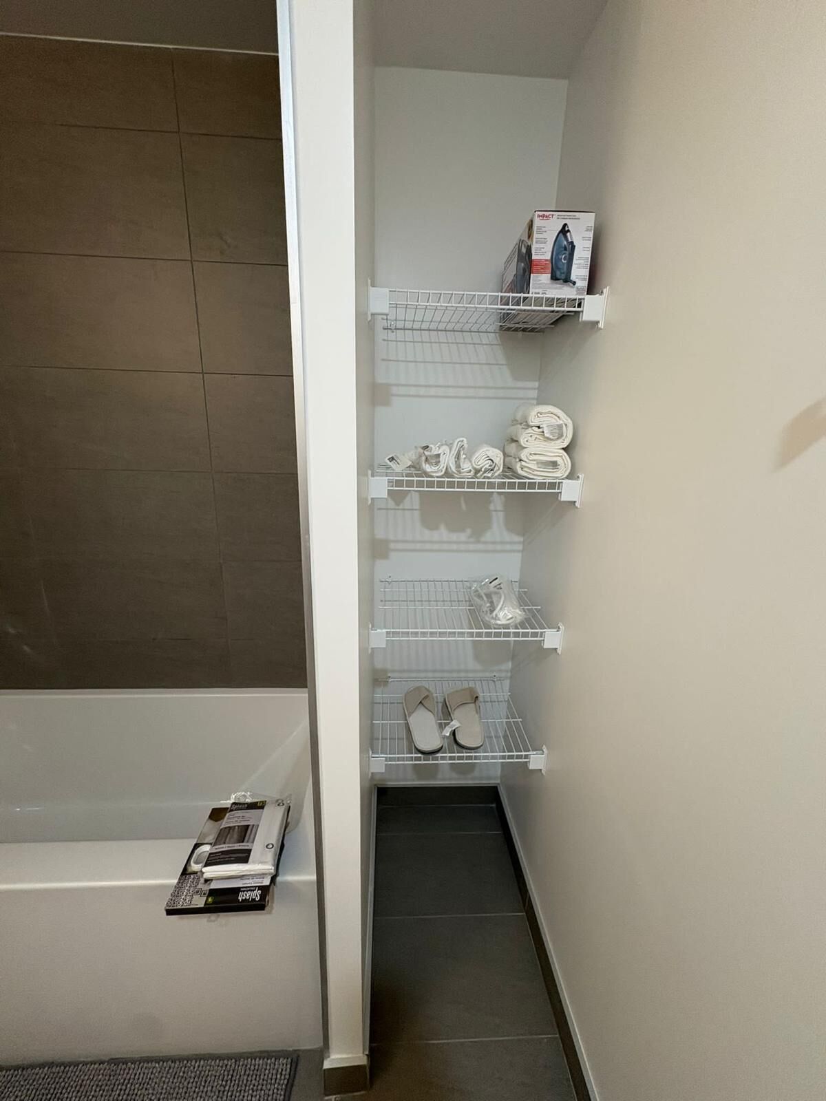 A bathroom with a shower, a toilet, and a storage unit with shelves.