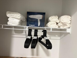 Un estante blanco con toallas dobladas con cuidado y una caja de secador de cerámica doble.