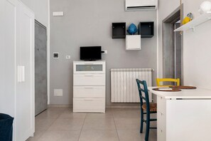 A compact room with a white cabinet, a flat-screen TV, a radiator, and a chair with a woven seat. - Holiday Home 'Vacanza Le Dune- Sole' with Private Terrace and Air Conditioning (Maruggio)