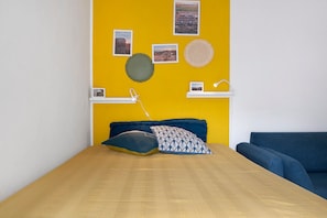 Una habitación con cama, sofá azul y pared amarilla decorada con marcos.