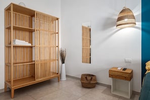 Una stanza con una grande libreria in legno, uno specchio, una lampada in vimini, un cesto di vimini e un piccolo tavolo con un dispositivo.