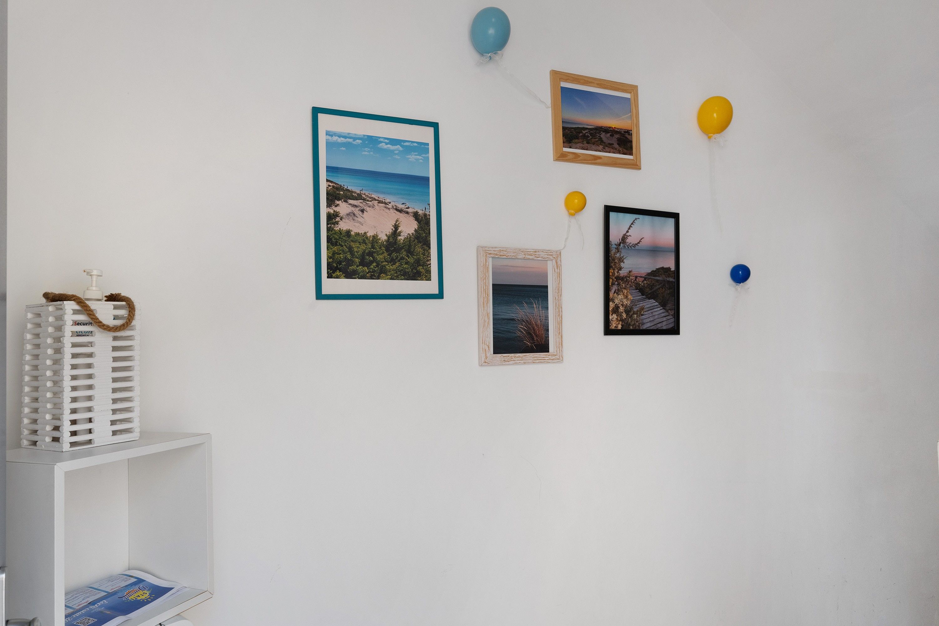 A wall with four framed photographs, a white shelf with a bottle, and a blue balloon.