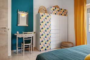 A bedroom with a bed, a desk with a chair, a wardrobe, and a mirror on the wall.