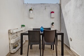 A small outdoor patio with a table and chairs, surrounded by white walls and potted plants.