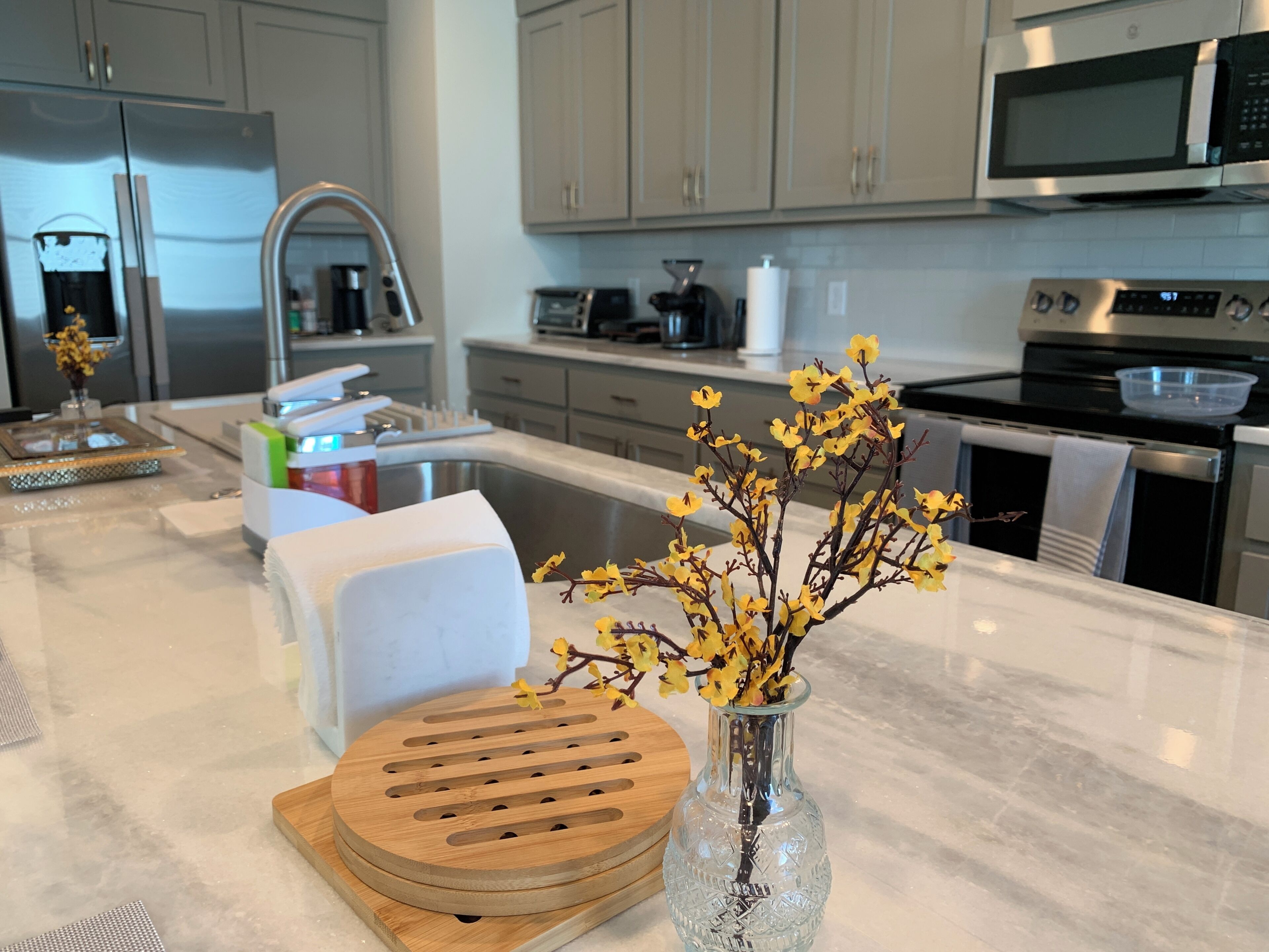 A modern kitchen with stainless steel appliances, a marble countertop, and a vase with yellow flowers.