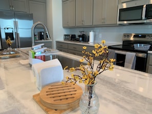 A modern kitchen with stainless steel appliances, a marble countertop, and a vase with yellow flowers. - Cozy Southern Retreat 3 (Oxford)
