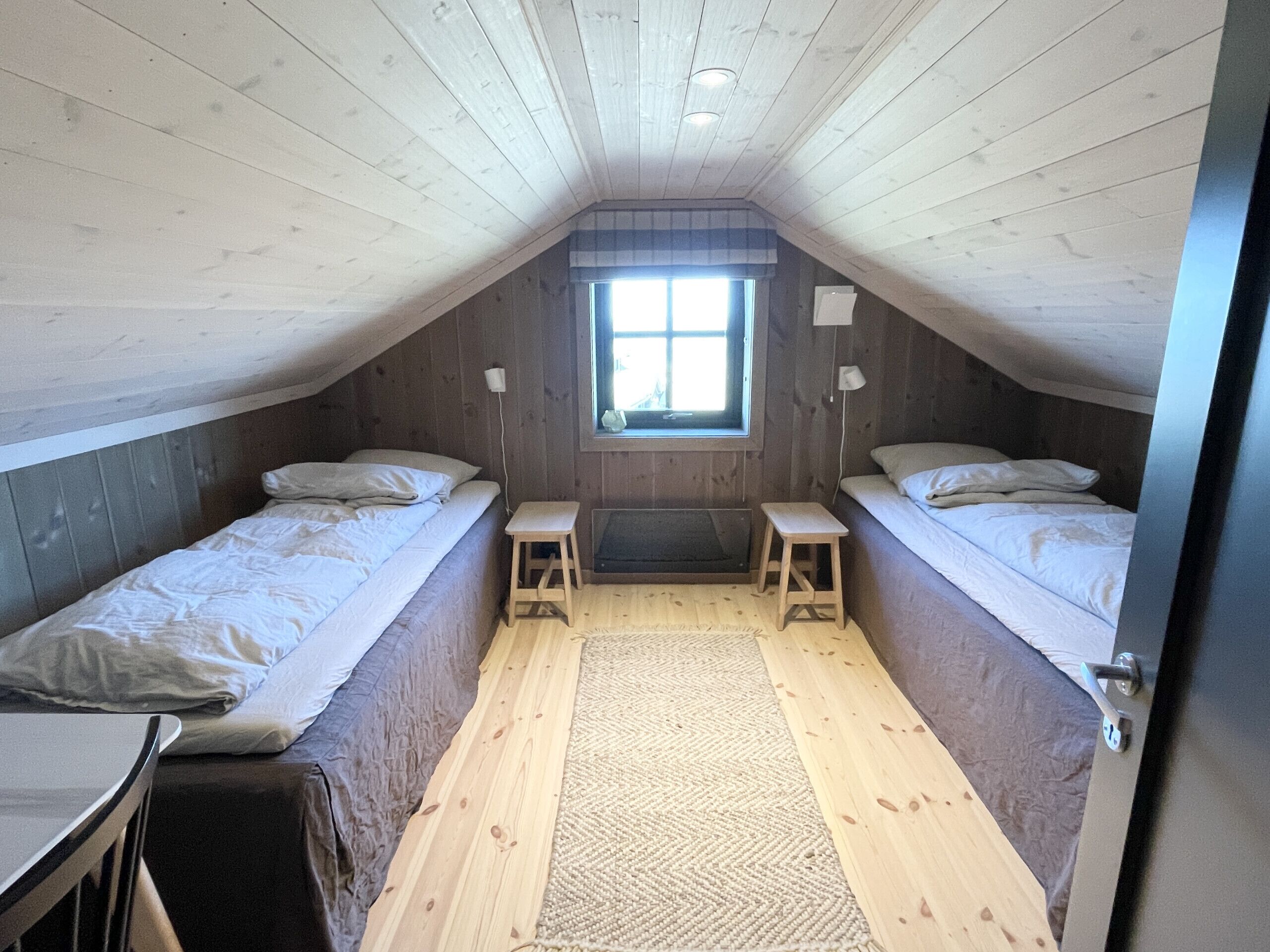 Une petite pièce de style mansardé, avec deux lits, une fenêtre et un plancher en bois.