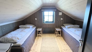 Une petite pièce de style mansardé, avec deux lits, une fenêtre et un plancher en bois.