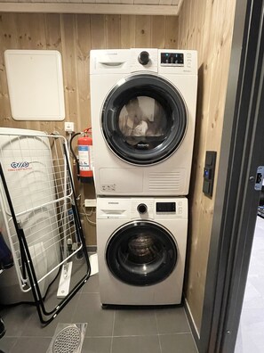 Un espace buanderie compact comprenant deux machines à laver superposées, un étendoir et un chauffe-eau.