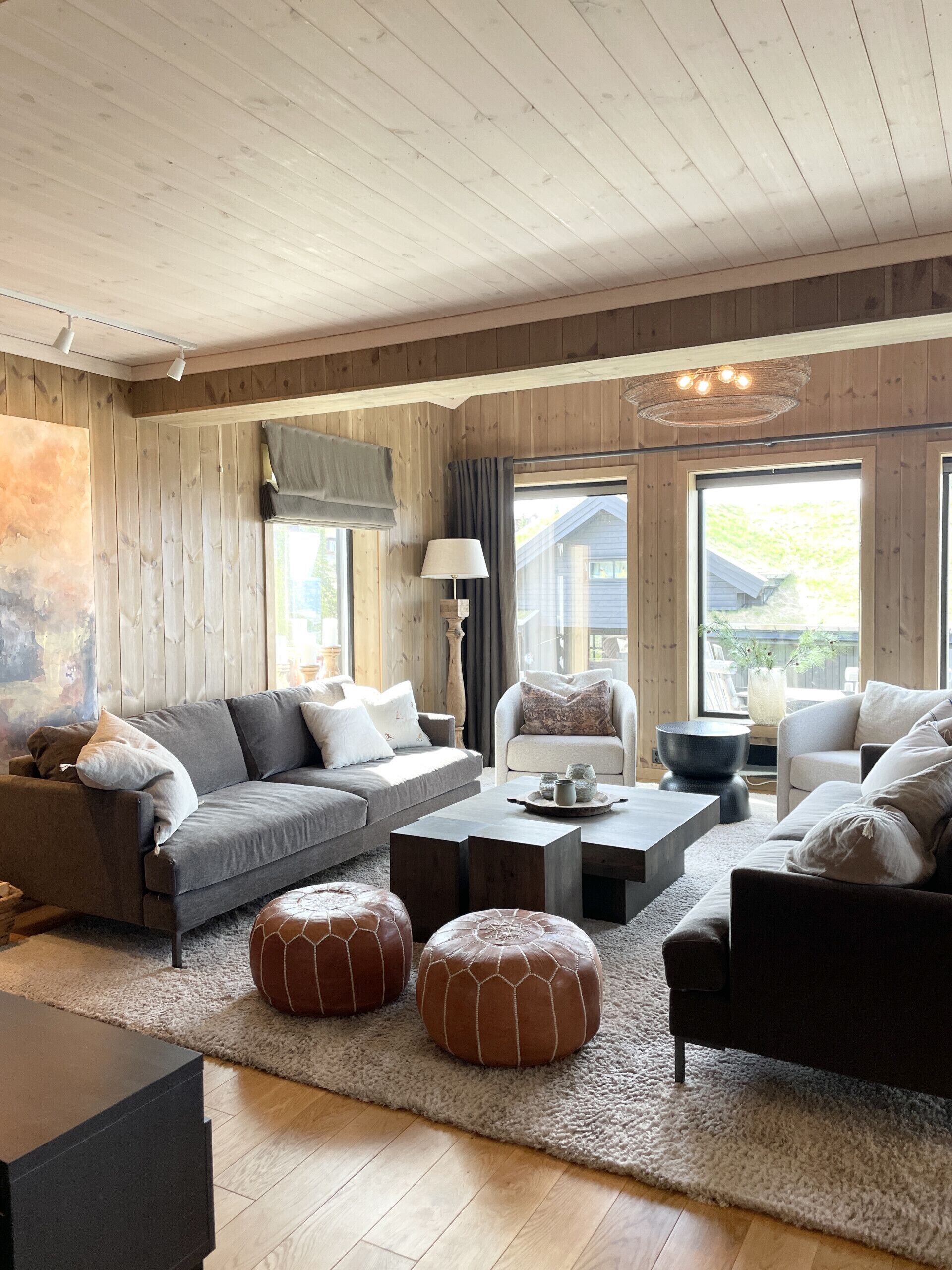 A cozy living room with a sofa, armchairs, ottomans, a coffee table, and a lamp.