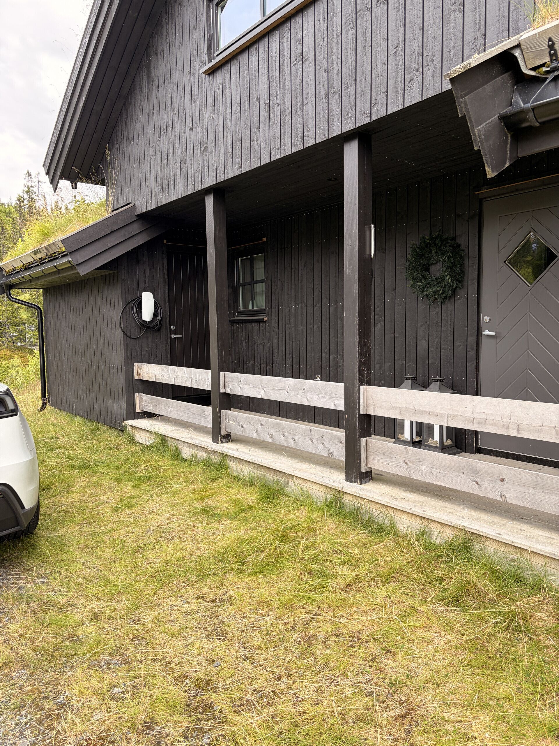 En toetages bygning med mørkt træfacade, en overdækket veranda og en hvid bil foran.