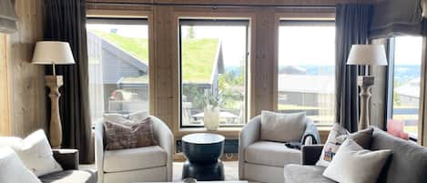 A cozy living room with wooden walls, large windows, and a central coffee table.
