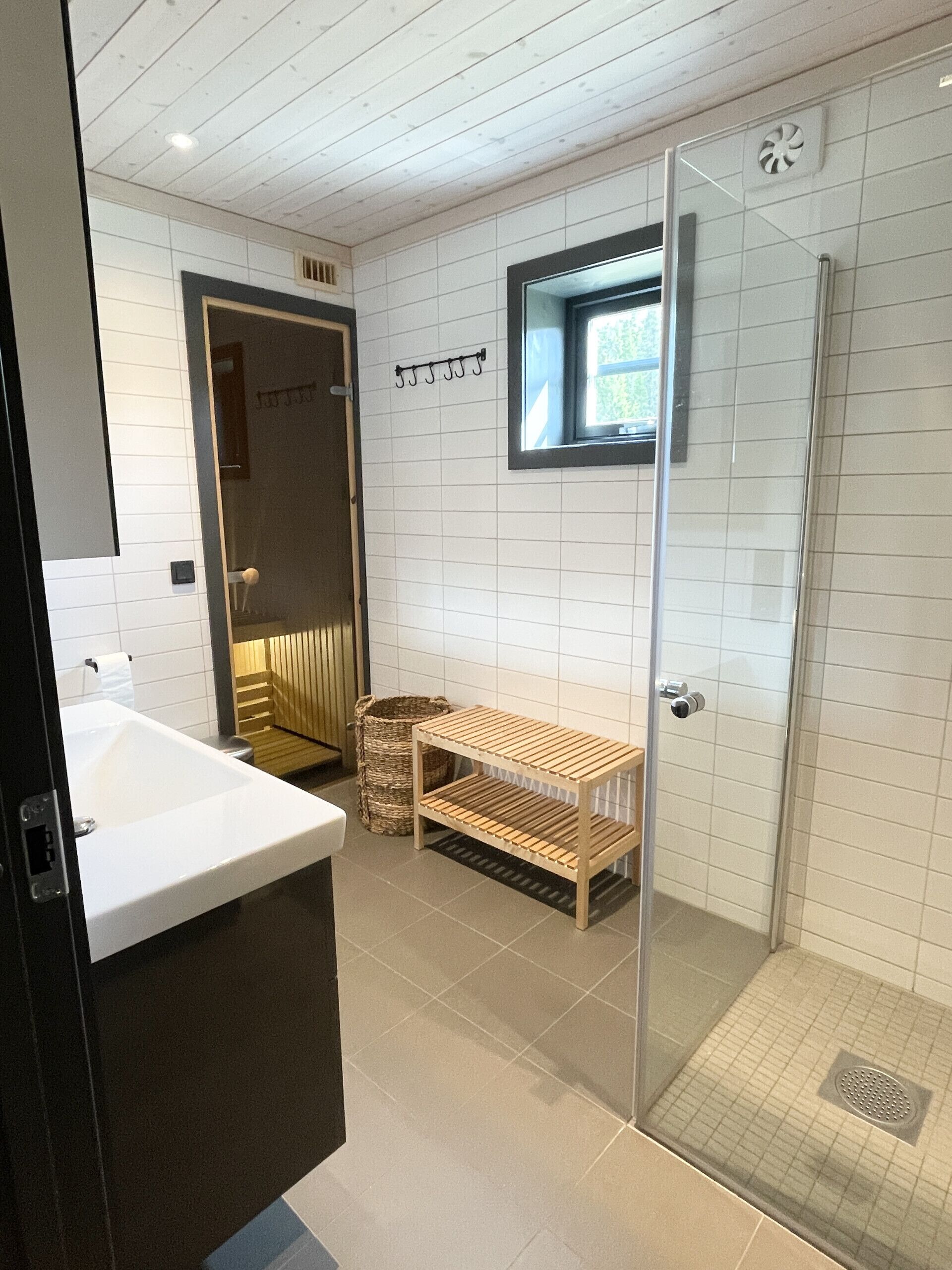 A modern bathroom with a glass shower enclosure, a wooden shelf, and a white sink.