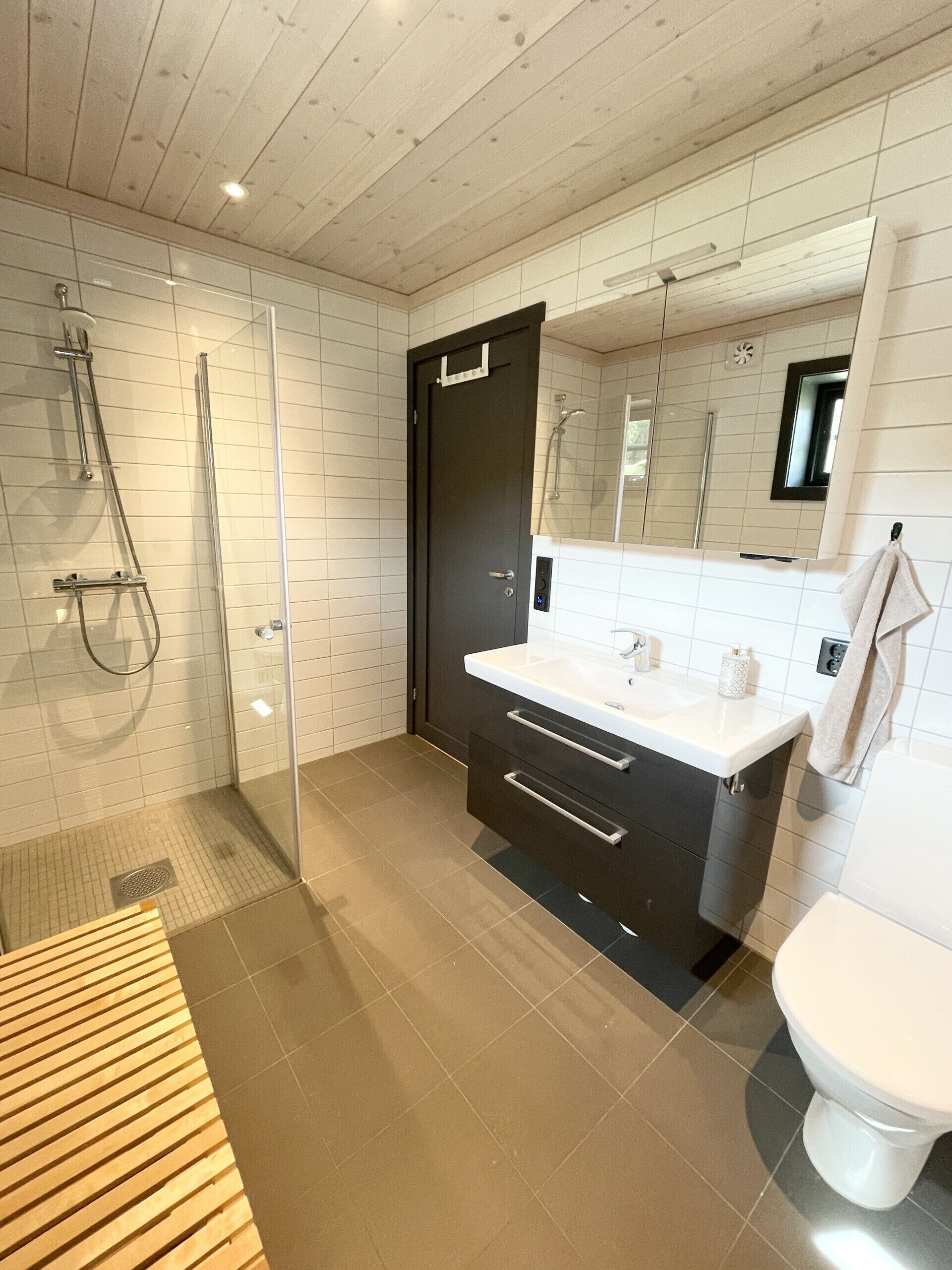 A modern bathroom with a glass-enclosed shower, a dark vanity with a white countertop, and a white toilet.