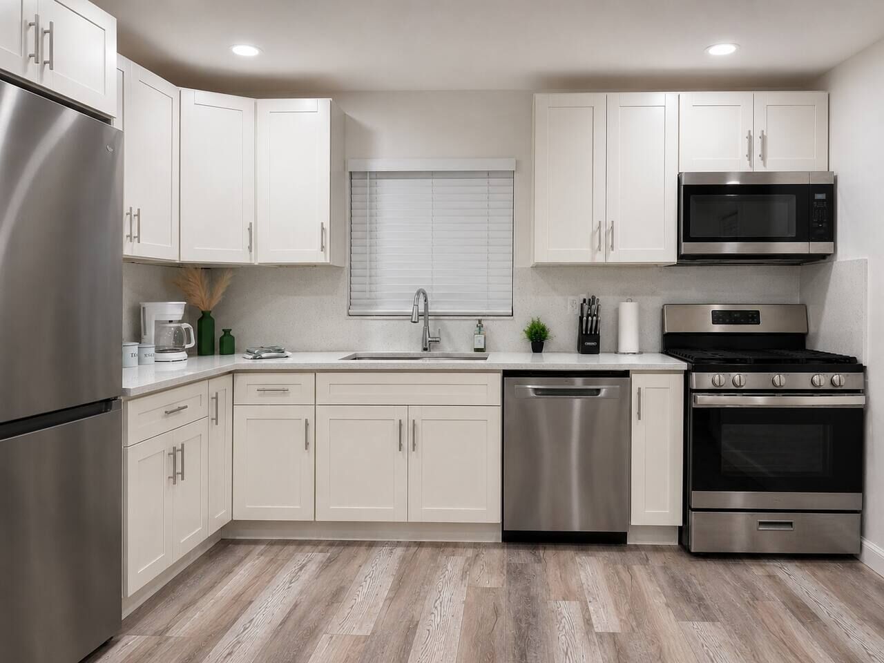 Una cucina moderna con elettrodomestici in acciaio inossidabile, mobili bianchi e pavimento in legno.