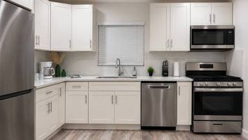 Una cucina moderna con elettrodomestici in acciaio inossidabile, mobili bianchi e pavimento in legno.
