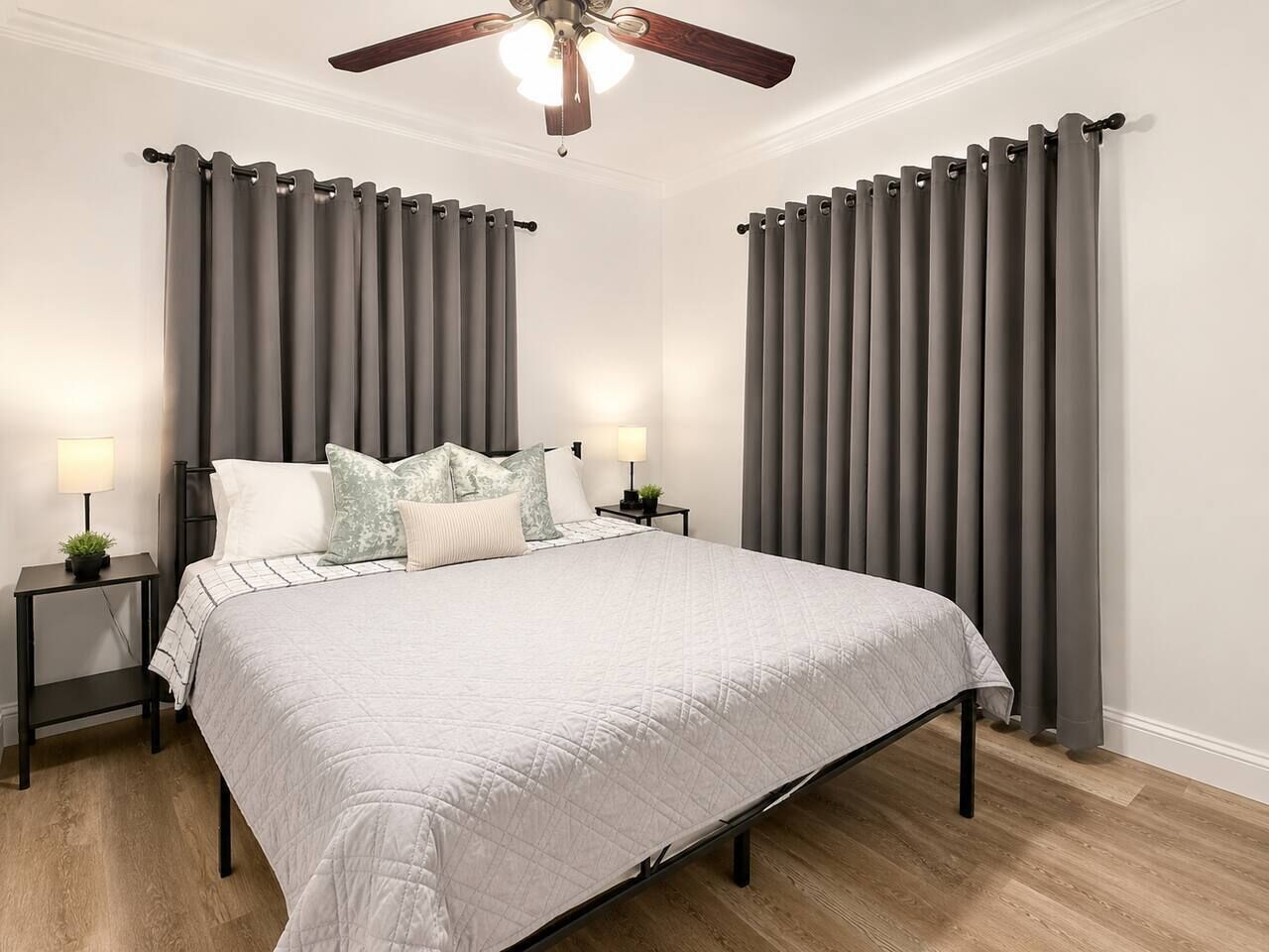 A bedroom with a bed, two bedside tables, a ceiling fan, and grey curtains.