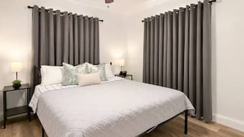 Una camera da letto con un letto, due comodini, una ventola a soffitto e tende grigie.