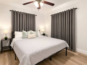 Ein Schlafzimmer mit einem Bett, zwei Nachttischen, einem Deckenventilator und grauen Vorhängen.