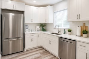 Eine moderne Küche mit Edelstahlgeräten, weißen Schränken und einem Fenster mit Jalousien.