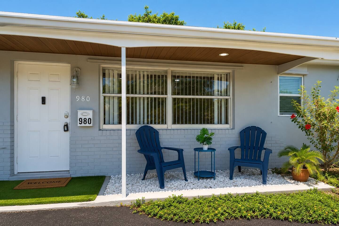 Una casa con una porta bianca, due sedie blu, un tavolino e una pianta in vaso.