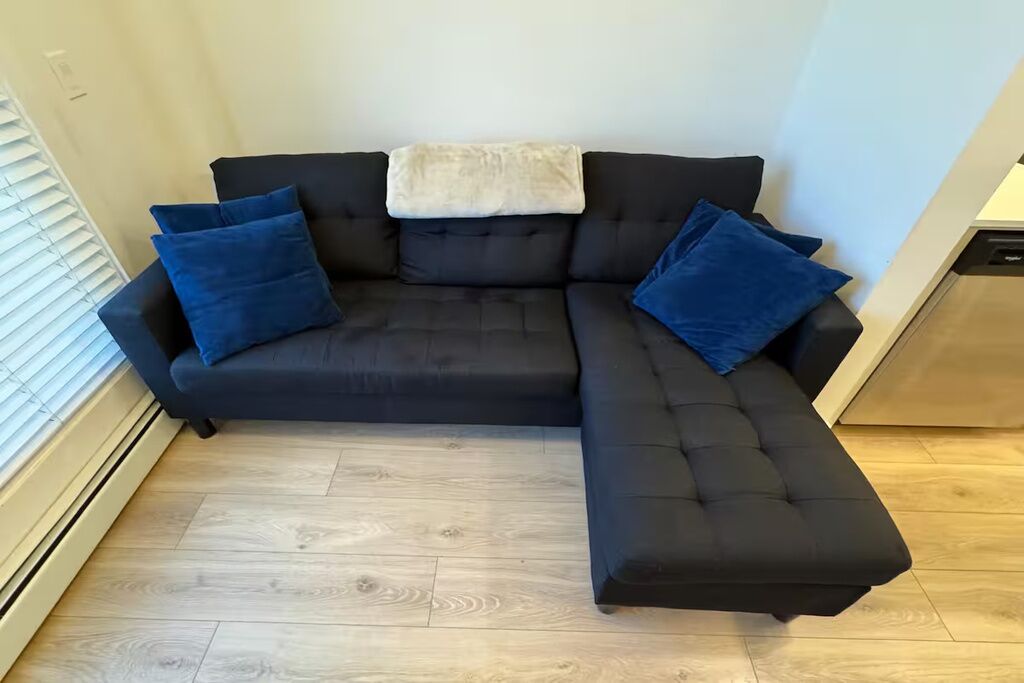 Un canapé d’angle noir avec trois coussins bleus et un plaid blanc.