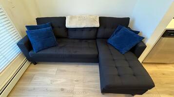 Un canapé d’angle noir avec trois coussins bleus et un plaid blanc.