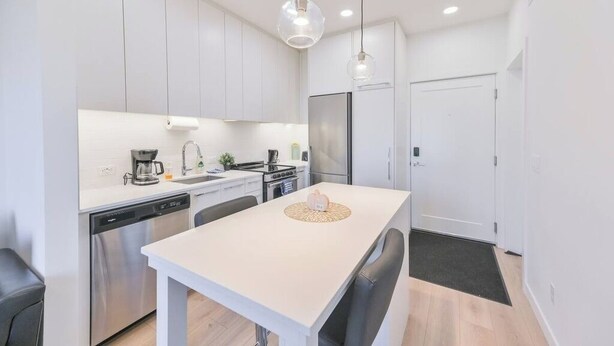 Une cuisine moderne avec des armoires blanches, des appareils en acier inoxydable et des luminaires suspendus.