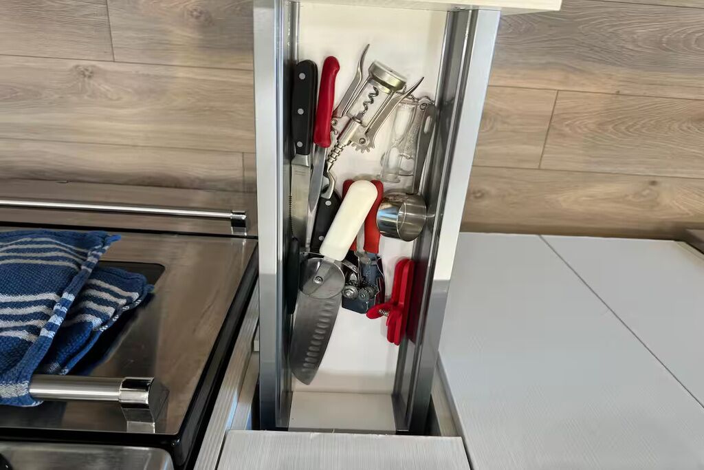 A drawer with various kitchen utensils, including a knife, a can opener, and a bottle opener.